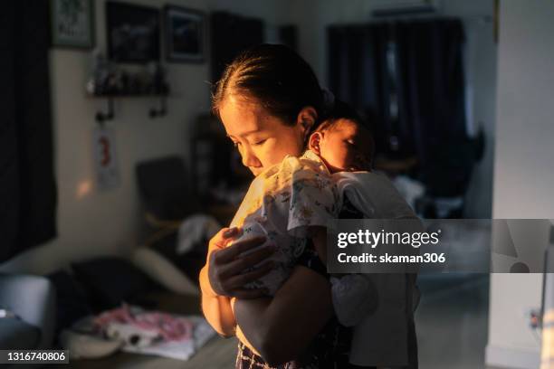 asian single mother comforting her infant daughter at home after feeding and burped - burping stock pictures, royalty-free photos & images