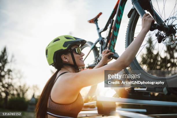 young woman attaching a mountain bike on a roof carrier on a car. - auto accessories stock pictures, royalty-free photos & images