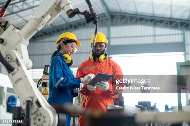 multi-ethnic software engineers explaining or discussion to controlling robotic welding process on digital tablet together at production line in a factory. - black jumpsuit stock pictures, royalty-free photos & images