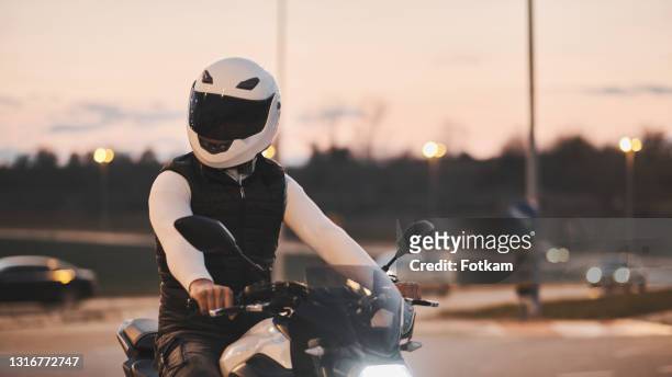 verticale d’un jeune homme s’asseyant sur la moto et utilisant une veste et un casque en cuir. - biker photos et images de collection