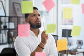 Shot of a young businessman brainstorming with sticky notes on a glass wall in an office