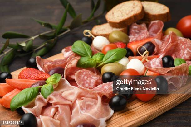 typical antipasto in an italian restaurant salami, ham prosciutto, with green and black olives, appetizers with mozzarella balls, cherry tomatoes - salami stock pictures, royalty-free photos & images
