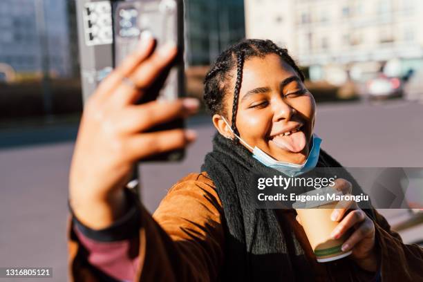 woman sticking out tongue taking selfie outdoors - high collar fotografías e imágenes de stock