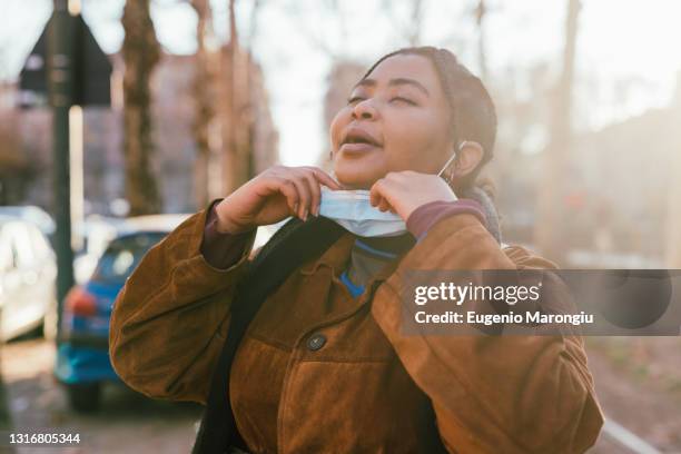 young woman removing face mask outdoors - taking off coat stock pictures, royalty-free photos & images