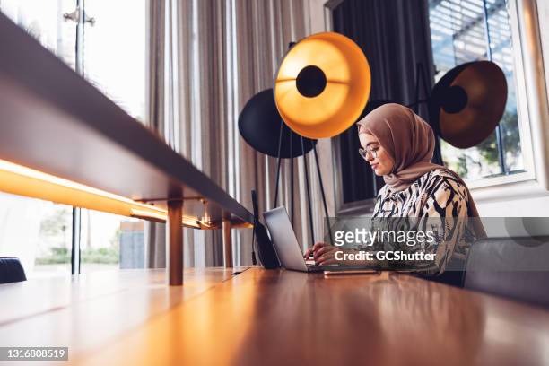 middle eastern girl working on a laptop from a luxury hotel lounge - middle east stock pictures, royalty-free photos & images
