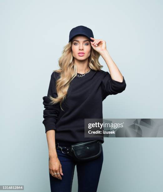 femme blond élégant posant au-dessus du fond gris - casquette de baseball photos et images de collection