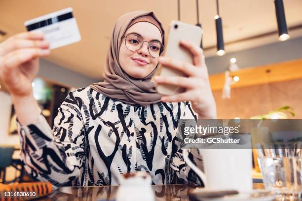 middle eastern girl mit kreditkarte, um online-käufe zu tätigen - arabische frau kopftuch stock-fotos und bilder