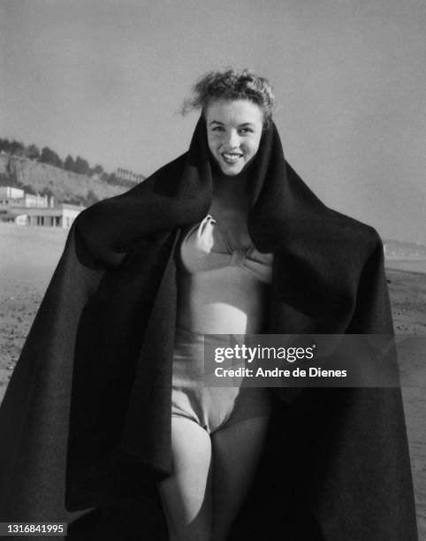 Portrait of American actress and model Marilyn Monroe as she poses, in a two-piece swimsuit and with a blanket over her shoulders, at Zuma Beach's...