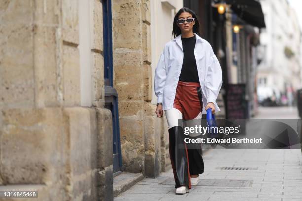 Melanie Darmon wears sunglasses from Loewe, a white opened oversized shirt, a black top, brown white and black flared leather pants from Stieglitz,...