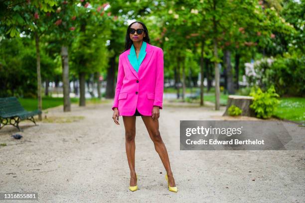 Emilie Joseph @in_fashionwetrust wears sunglasses, a two-tone oversized colorblock blazer in neon pink and green, notched collar, worn as a dress,...