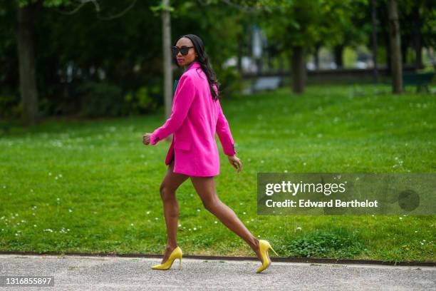 Emilie Joseph @in_fashionwetrust wears sunglasses, a two-tone oversized colorblock blazer in neon pink and green, notched collar, worn as a dress,...