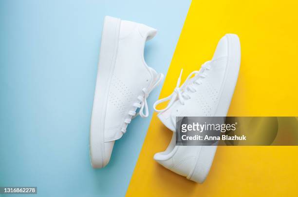 white sports shoes over blue and yellow background, sports and casual clothing 90s' style concept. - white shoe fotografías e imágenes de stock