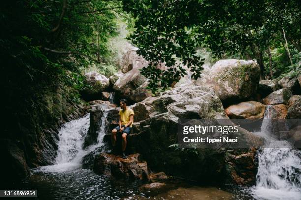 man sitting on rock by waterfall in forest - outdoor guy sitting on a rock stockfoto's en -beelden