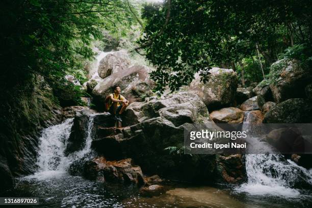 man sitting on rock by waterfall - outdoor guy sitting on a rock stockfoto's en -beelden