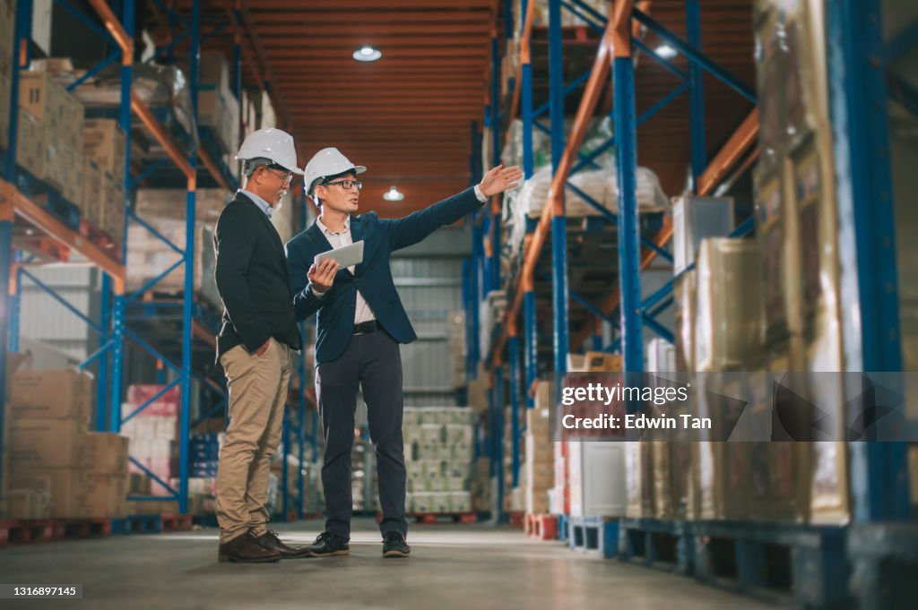 Asian chinese management having discussion at warehouse with white hardhat using digital tablet