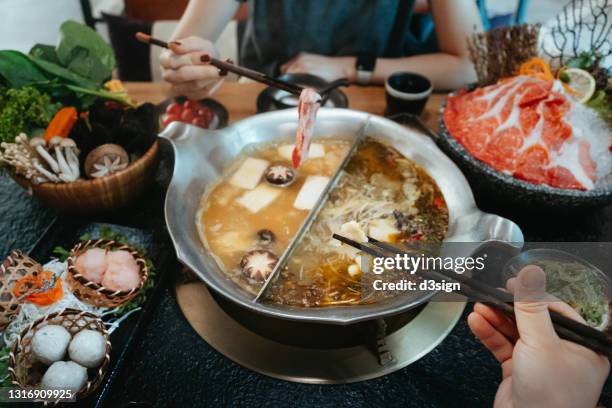 personal perspective of asian couple having a good time, enjoying traditional chinese hotpot with assorted fresh and scrumptious ingredients in restaurant. chinese cuisine and food. eating out lifestyle - hot pot dish fotografías e imágenes de stock