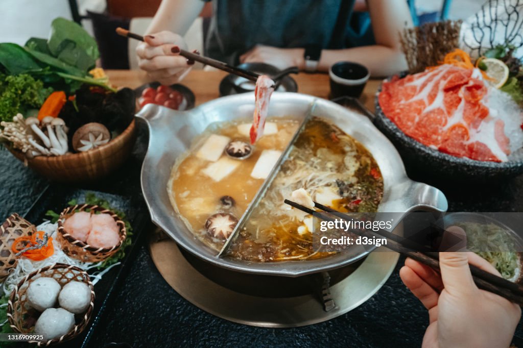 Personal perspective of Asian couple having a good time, enjoying traditional Chinese hotpot with assorted fresh and scrumptious ingredients in restaurant. Chinese cuisine and food. Eating out lifestyle