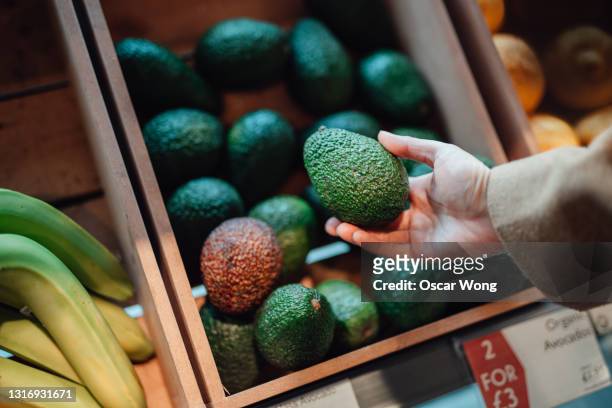 close up shot of woman’s hand holding avocado in grocery store - avocat légume photos et images de collection