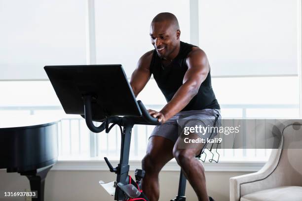 african-american man on exercise bike at home - spinning bikes stock pictures, royalty-free photos & images