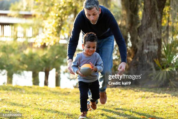 father with his mixed race son playing at the park - american football family stock pictures, royalty-free photos & images