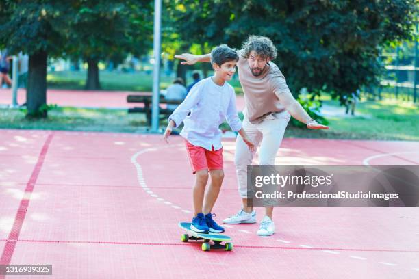 happy father is helping his son to learn to ride a long board. - father longboard stock pictures, royalty-free photos & images