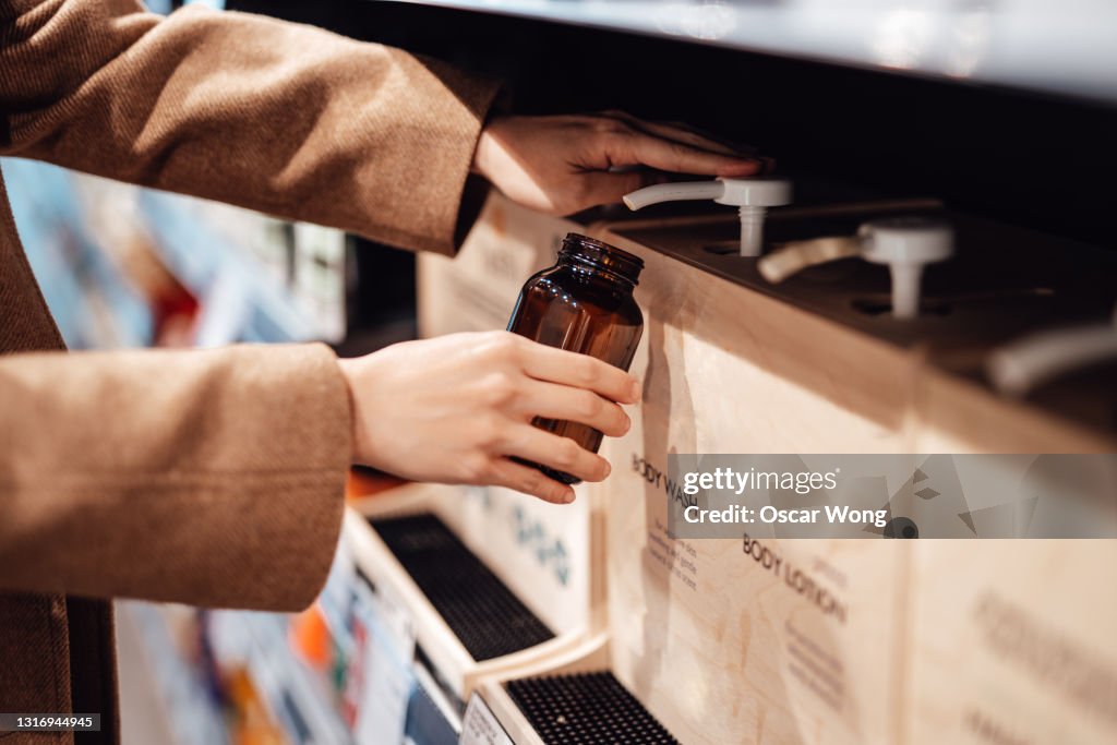 Young woman refilling shower gel into a reusable glass bottle in zero waste store