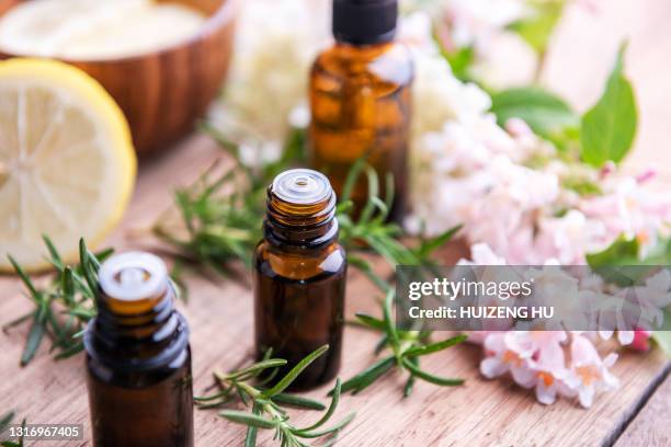 bottles of essential oil with herbs and fruits on wooden table: rosemary, lemon and flowers - essence 個照片及圖片檔