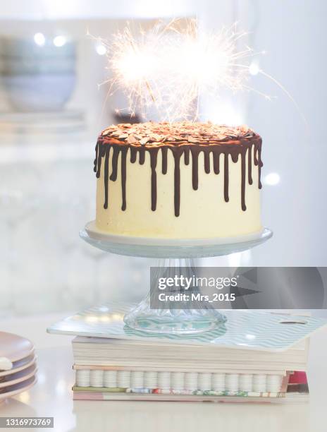 vanilla birthday cake with chocolate ganache, glaze,  and sparklers on a cake stand in a  kitchen - cakestand stock-fotos und bilder