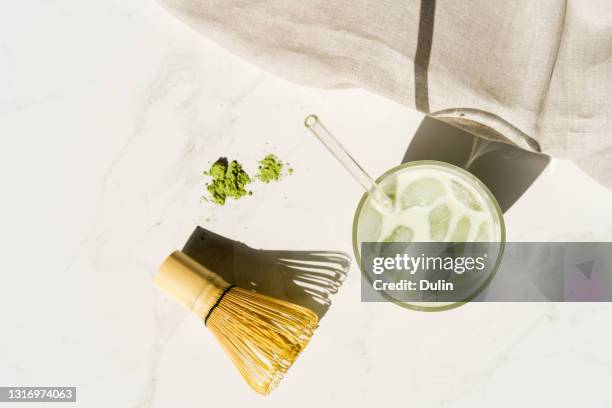 overhead view of an iced matcha green tea drink next to matcha powder, bamboo whisk and spoon - matcha tea stock pictures, royalty-free photos & images