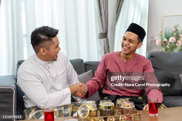 two men shaking hands during hari raya eid ul fitr celebration - baju melayu, malay traditional clothing - baju melayu stock pictures, royalty-free photos & images