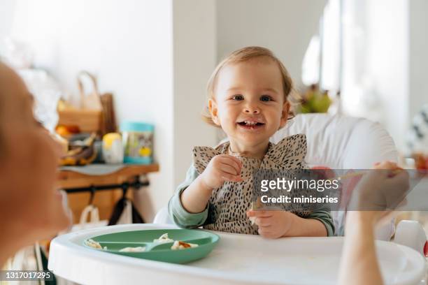 fröhliche baby-mädchen essen mahlzeit mit mutter - baby stock-fotos und bilder