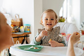 Cheerful baby girl eating meal with mother