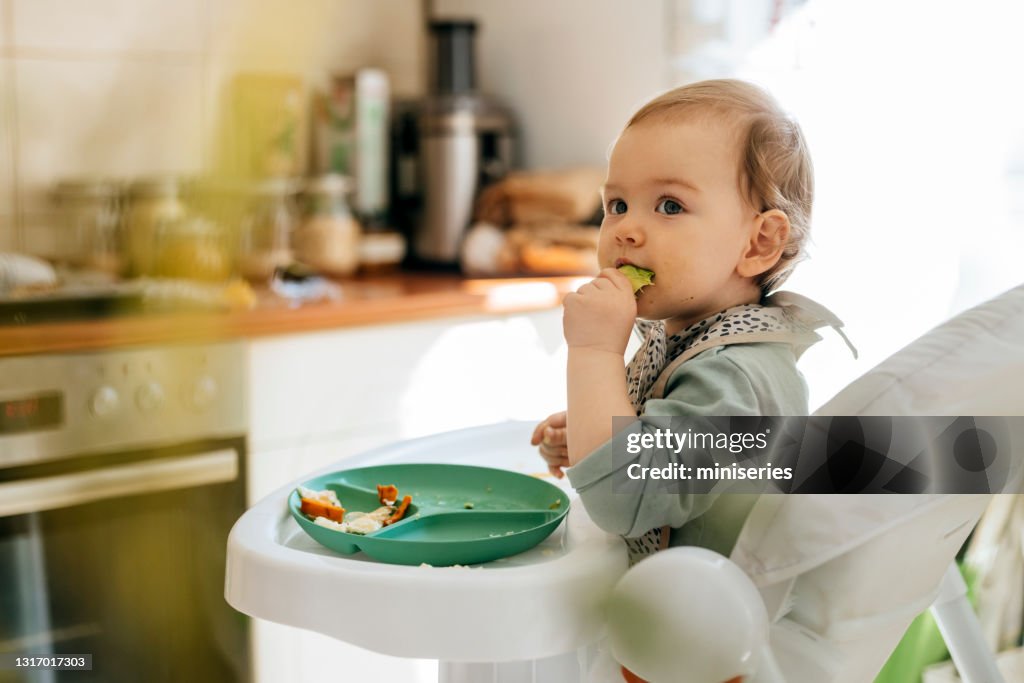 Nettes Baby Mädchen essen Mahlzeit auf Hochstuhl