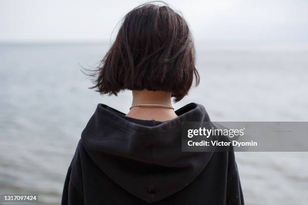 young brunette in the black hood o the shore - zelfmoord stockfoto's en -beelden