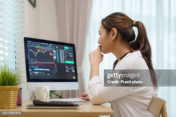 asian woman are sitting at their desks at home trading stocks or cryptocurrency. in the living room at home. people handling various aspects of their finances from home. - 財經職業 個照片及圖片檔
