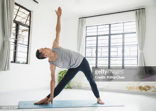 asian man practicing yoga in a yoga studio-triangle position - yoga studio stock-fotos und bilder