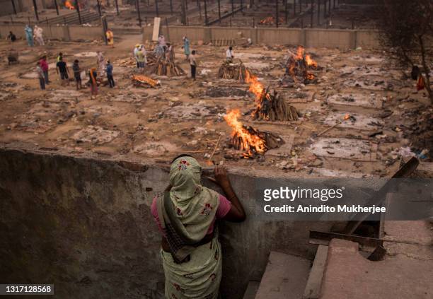 Lady looks at the burning funeral pyres of the patients who died of the Covid-19 coronavirus from her house near a makeshift crematorium on May 09,...