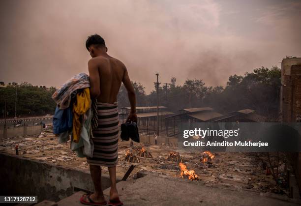 Man does his household chores on the backdrop of burning funeral pyres of the patients who died of the Covid-19 coronavirus at a crematorium on May...