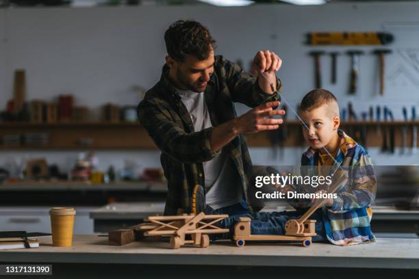 boy and his father in carpenter workshop playing with wooden toy - fathers day tools stock pictures, royalty-free photos & images