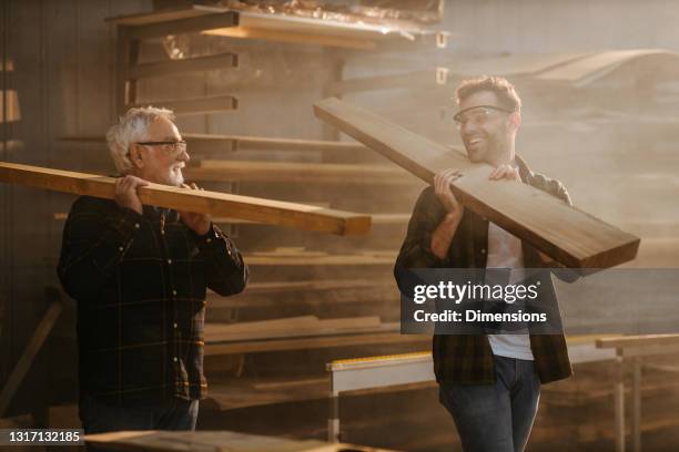 vater und sohn arbeiten mit einer planke in der werkstatt - father son business europe stock-fotos und bilder