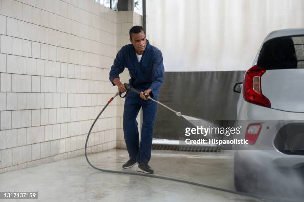 mens die bij een autowasserette werkt die een voertuig met een slang schoonmaakt - car wash stockfoto's en -beelden