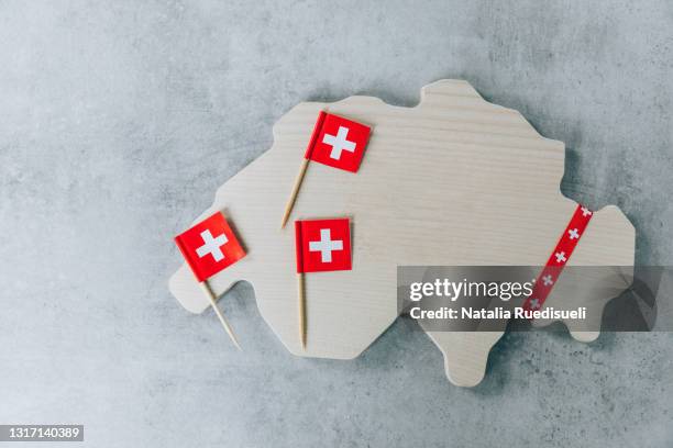 wooden cutting board with swiss flags in the shape of switzerland on gray background. - swiss flag fotografías e imágenes de stock