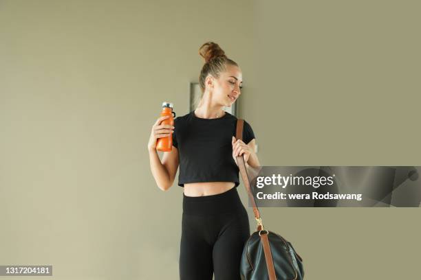 healthy woman wearing exercise clothes carry sports bag and water bottle while walking - gym bag stock-fotos und bilder