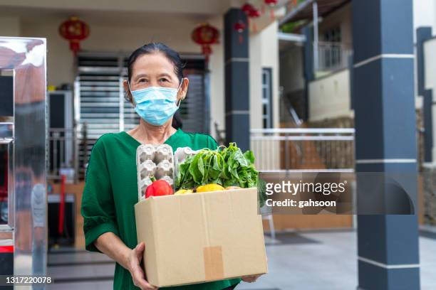 senior woman with facemask is grateful for food delivery from helpful volunteer during covid-19 - foodbanks for the needy stock pictures, royalty-free photos & images