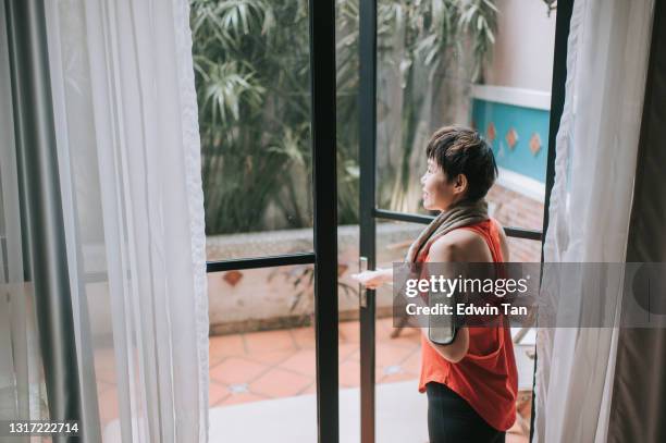 sideview aziatische chinese mid volwassen vrouw open deur en lopen naar haar achtertuin voor training met handdoek glimlachen - open workouts stockfoto's en -beelden