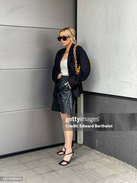 Justyna Czerniak wears a dark navy blue / black blazer jacket from Acne studios, a white low neck top from Sundarbay, black leather high heeled shoes...