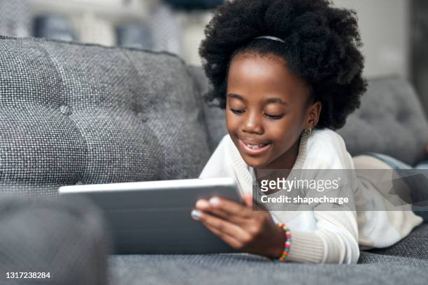 shot of an adorable little girl using a digital tablet while lying on the couch at home - tablet close up real copyspace stock pictures, royalty-free photos & images