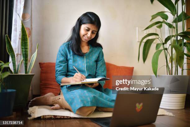 women writing in her diary while working on laptop - scriptwriter foto e immagini stock