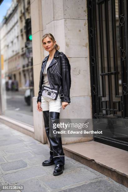 Xenia Adonts wears earrings, a necklace, a black leather padded biker jacket, a gray wool ribbed top, a Vuitton Petite Malle case bag, black and...