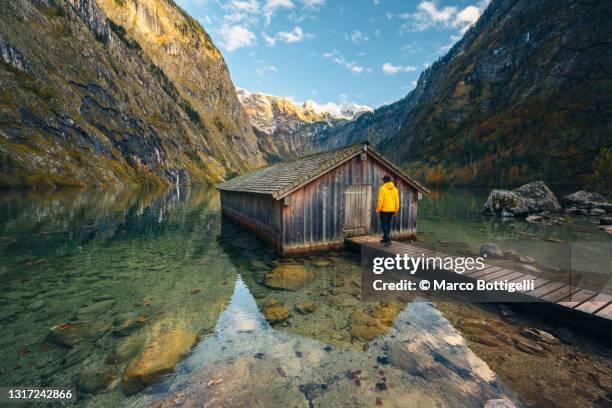 person walking towards a boathouse in mountain lake, germany - rimessa per barche foto e immagini stock